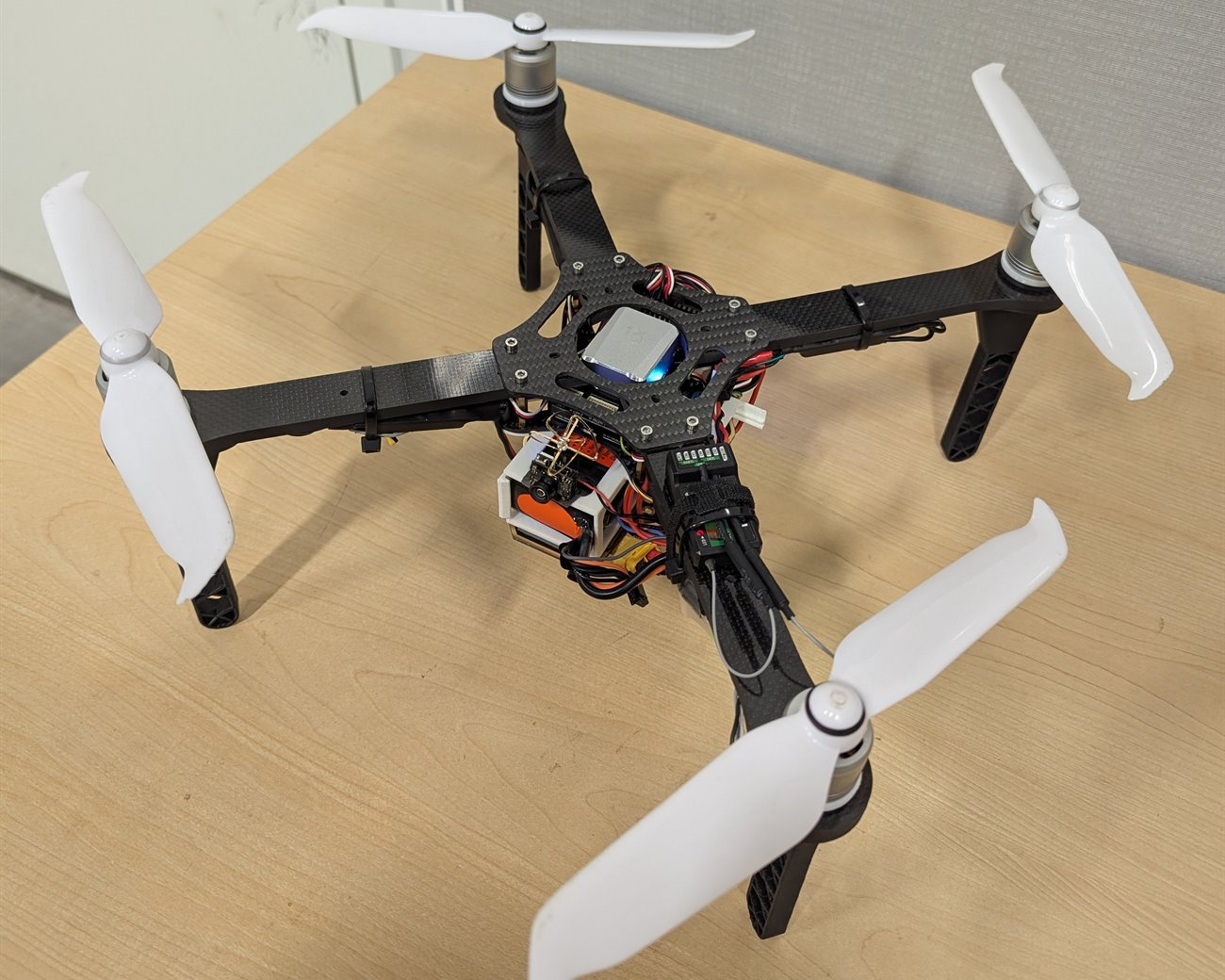 The finished carbon fiber quadcopter on a desk with a Pixhawk V6X and GPS mounted